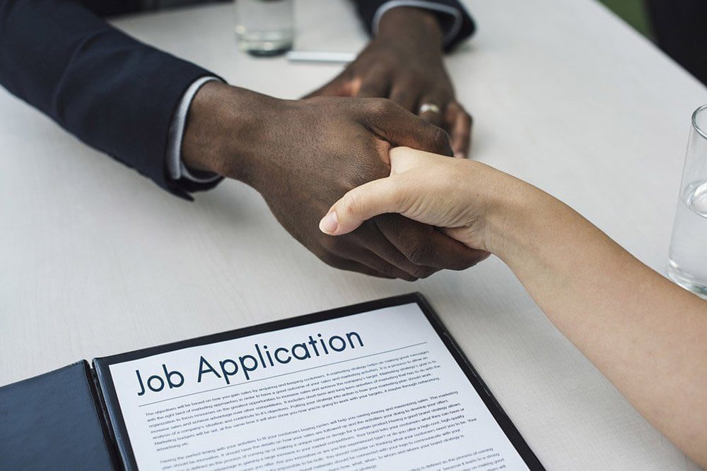 Two people shaking hands over a desk after agreeing a job offer.